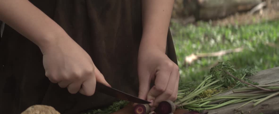 A girl cuts vegetables outside on a cutting board