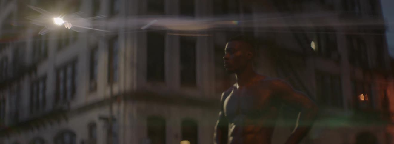 A shirtless man stands in a intersection at dusk