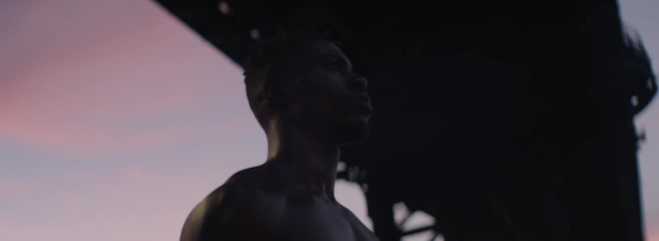 A shirtless man walks in a city at sunset