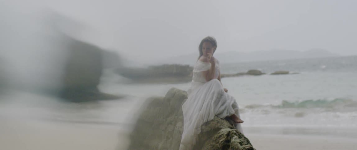 A woman sits on a rock on the beach