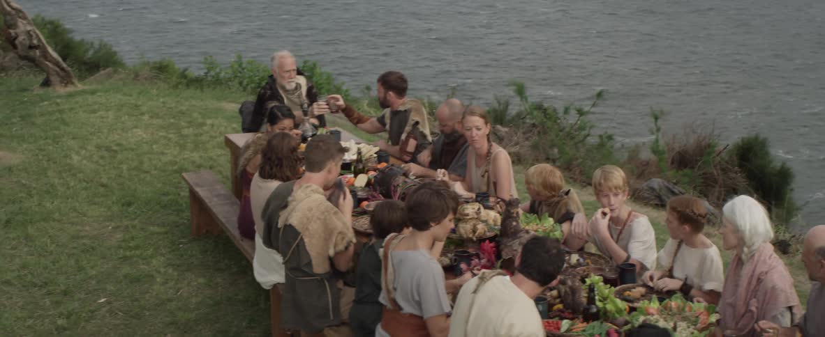 Large group of people eating at a table outside near the ocean