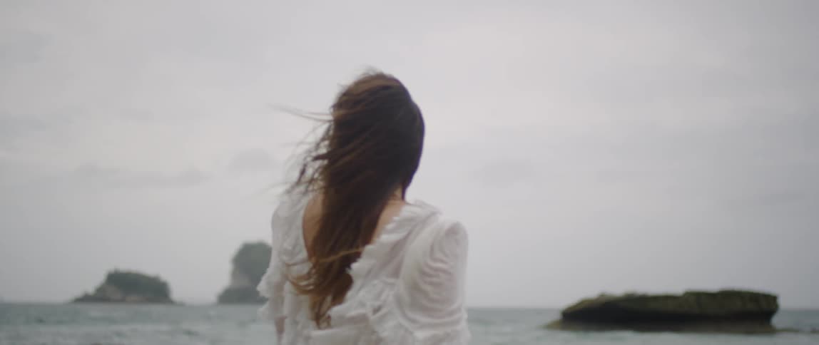 A woman dressed in white walks along the shoreline