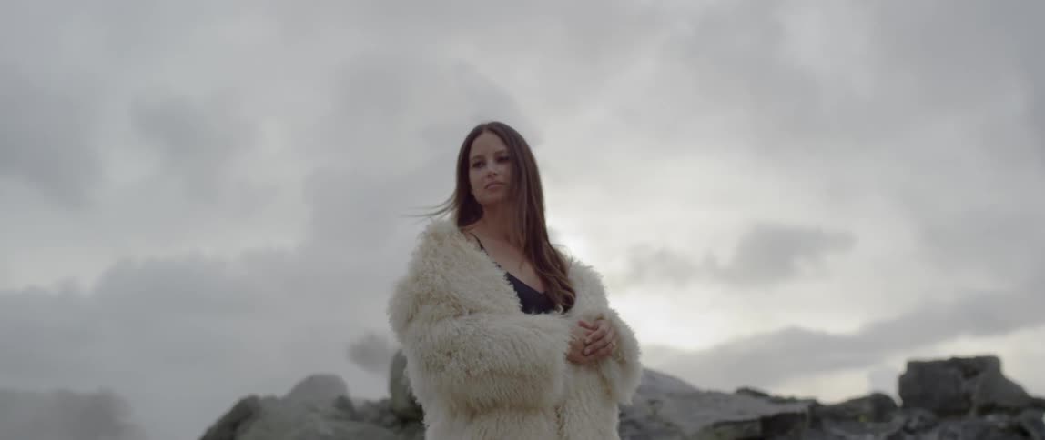 A woman wears a fur coat outside on a cloudy day