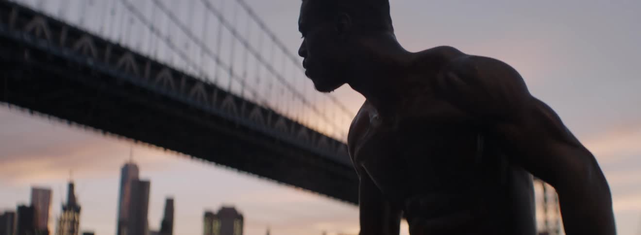 Man drinks a bottle of water near a bridge at sunset