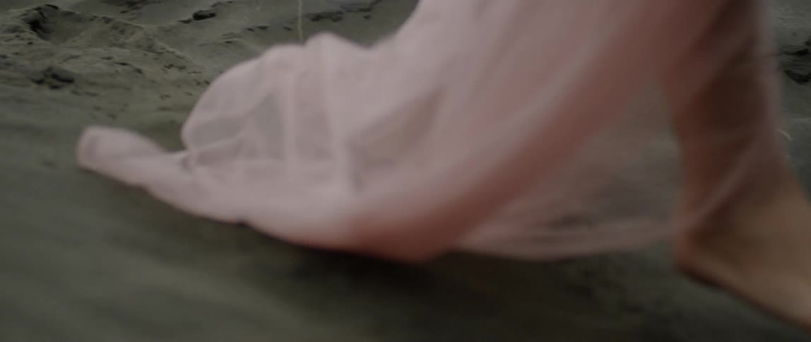 A woman walks through the sand wearing a pink dress
