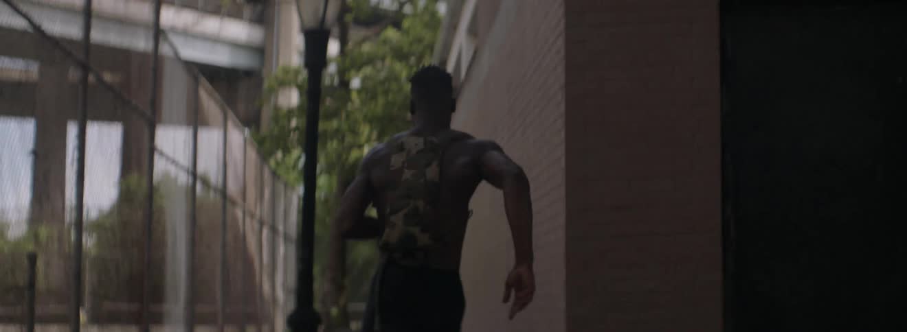 A male athlete is running past a building and fence in a city
