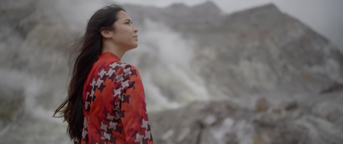A woman walks in the mountains as steam rises in the distance