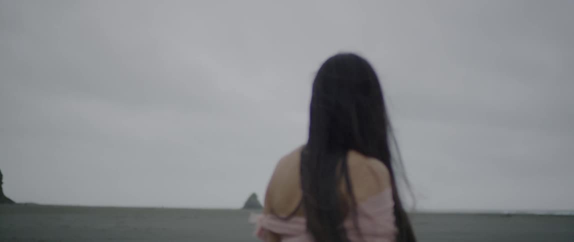 Woman with long black hair looks out at the ocean