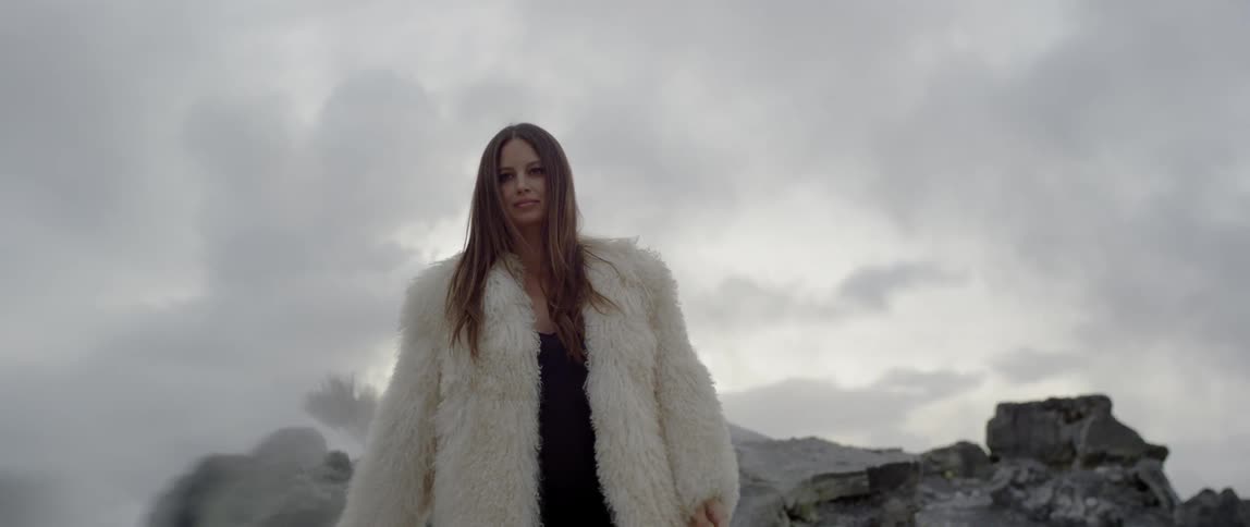 Woman wearing a white fur coat stands outside on a cloudy day