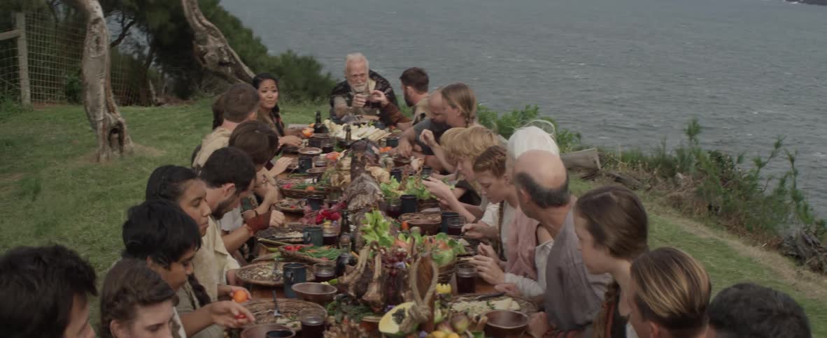 A large family sits at a table outside eating a meal