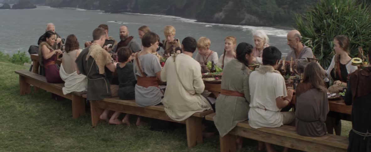 A family dines at an outdoor table on the coast