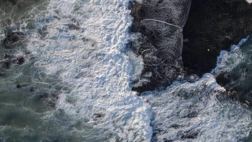 The waves crash against the rocks below