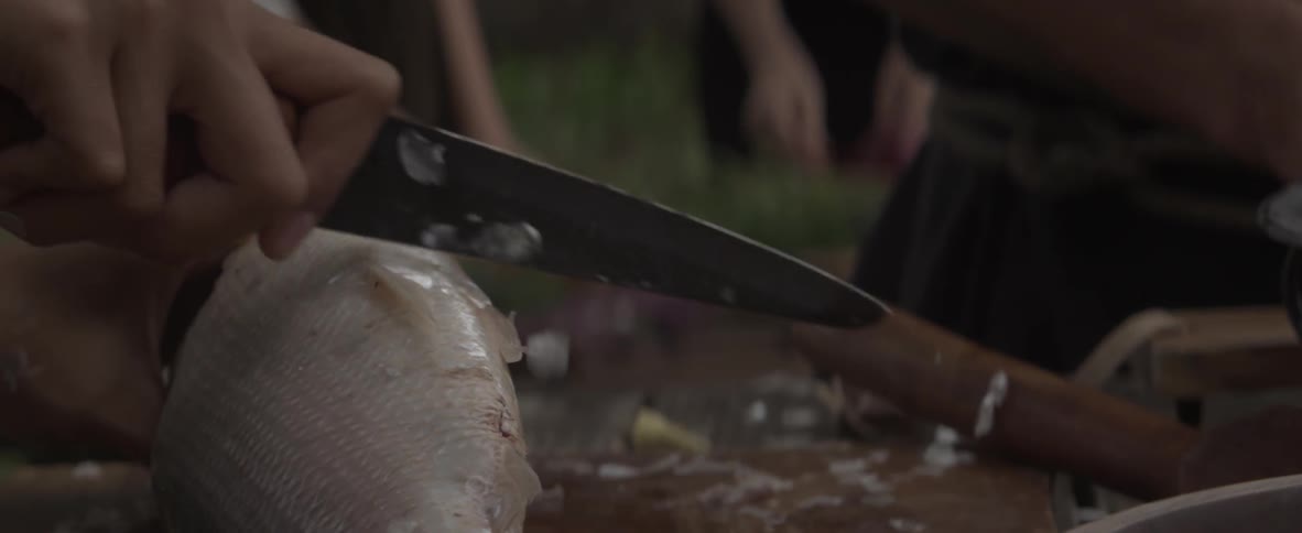 A person shaves fish scales with a knife