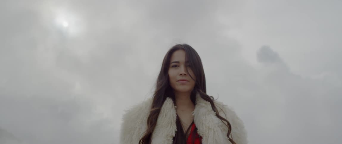 A woman stands outside in a fur coat on a cloudy day