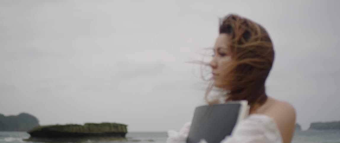 A woman is holding a book and walking on the beach