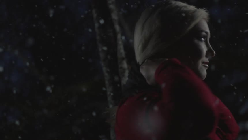 A woman is putting on a scarf outdoors at night while its snowing