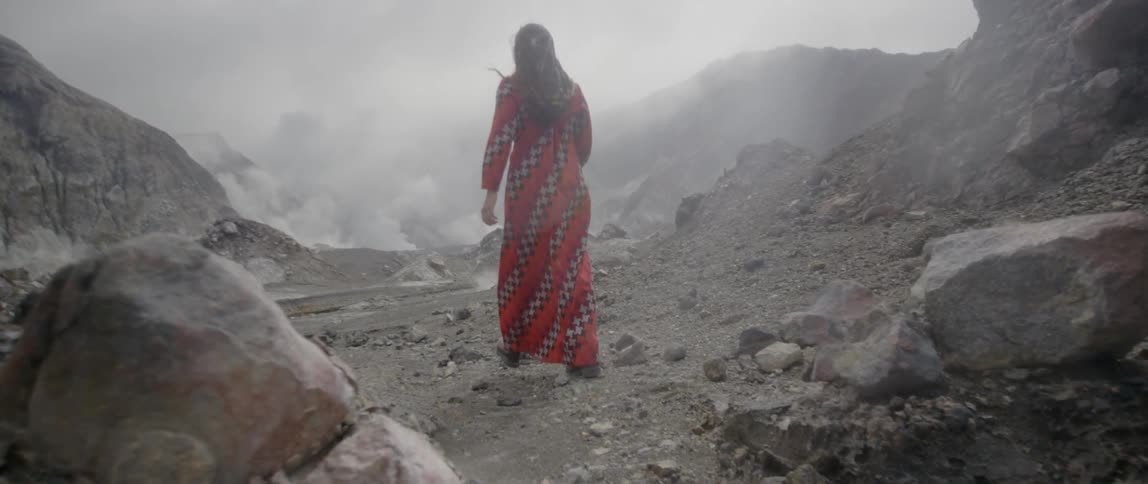 A woman in a red gown walks over a mountain