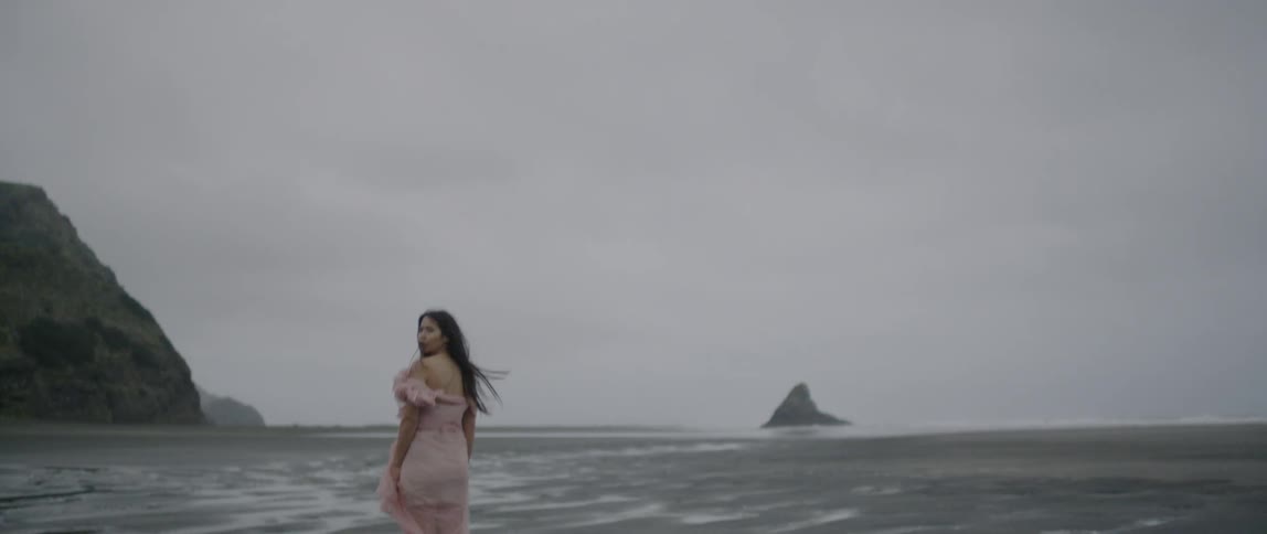 A woman wearing a dress stands on the sand as the wind blows