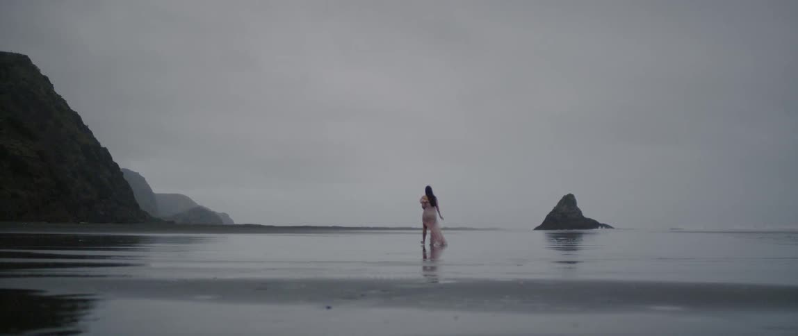 A woman walks along the beach beneath overcast skies
