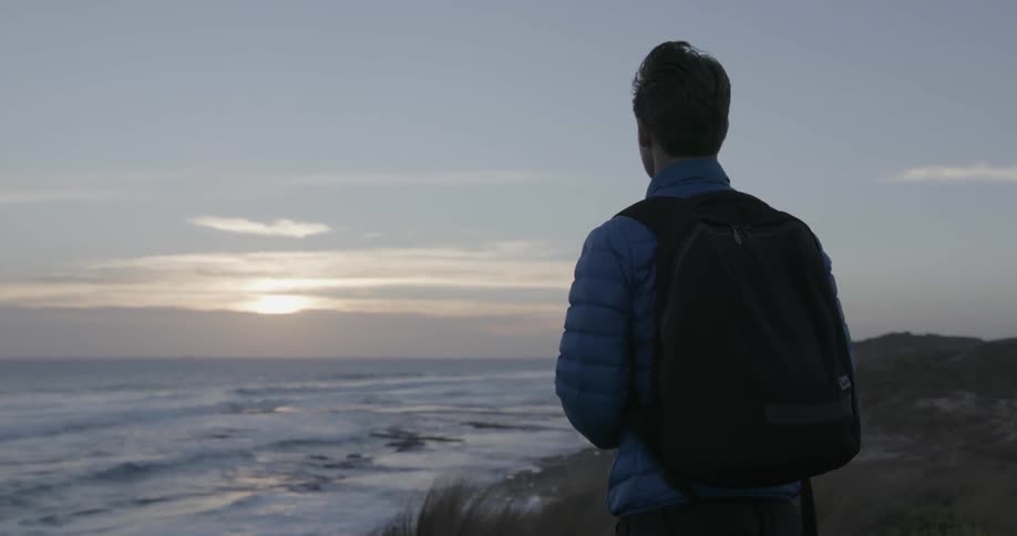 A man looks out at the ocean at sunset