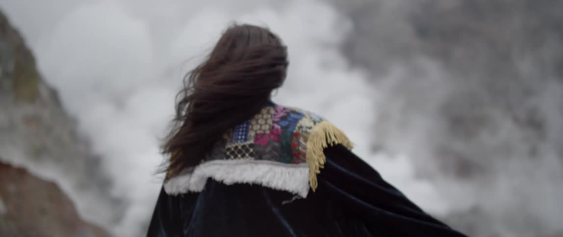 Woman with long hair sweeps her arm around under a cloudy sky