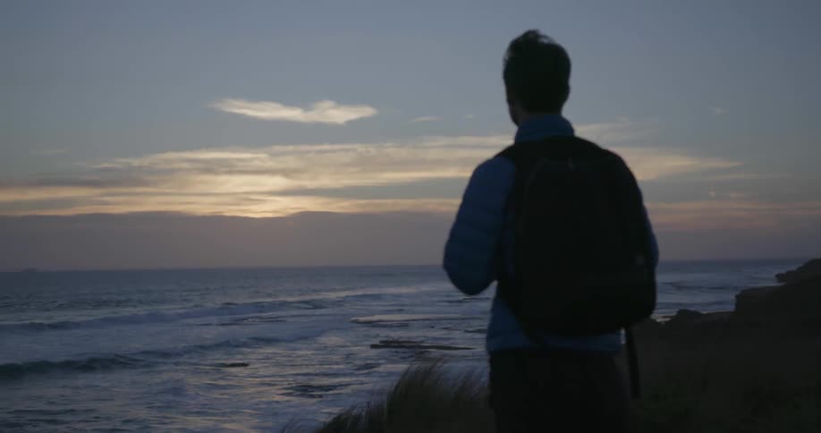 A man wearing a backpack looks out at the ocean
