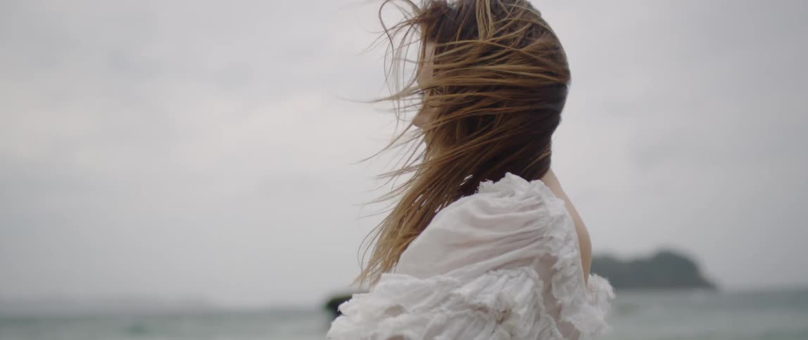A woman stands in the wind by the beach