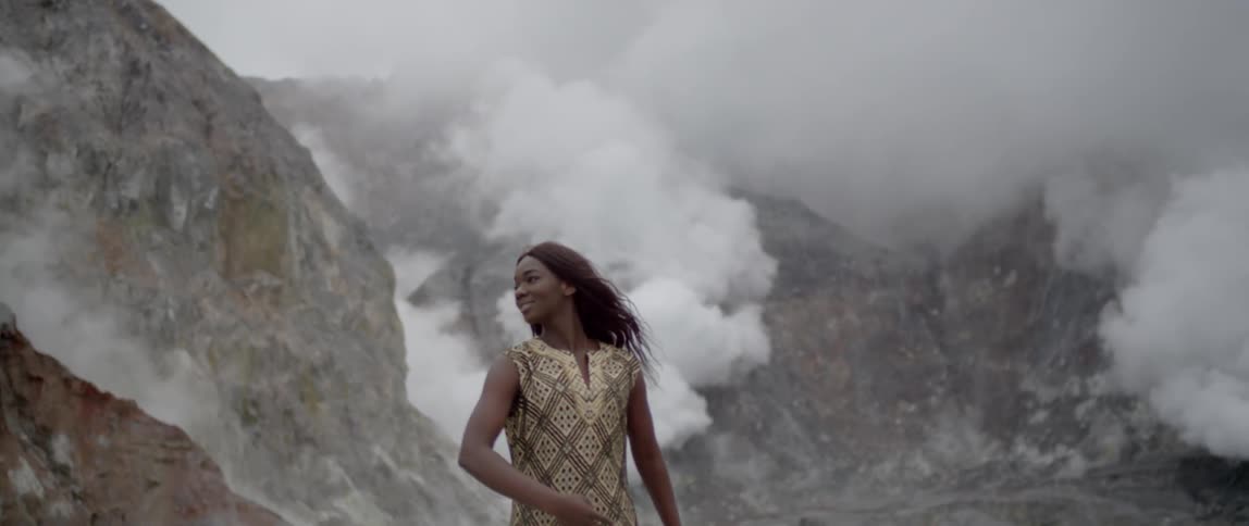 A woman walks outdoors in front of foggy mountains