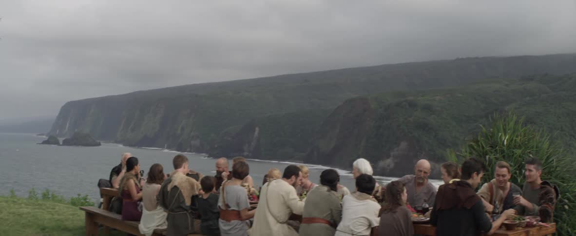 Large group of people eating at table outside overlooking ocean