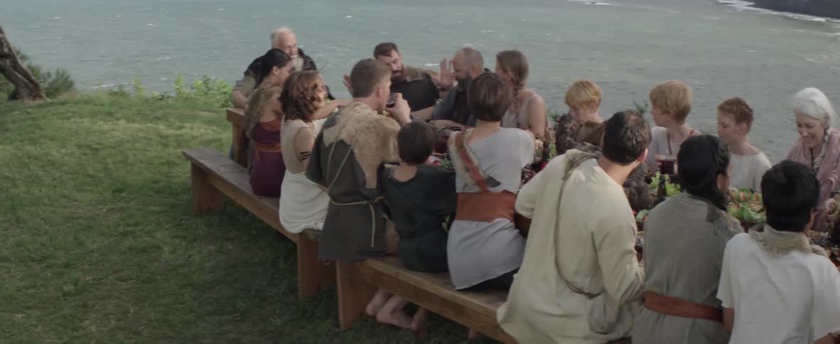 Large group of people eating at a table outside near the ocean