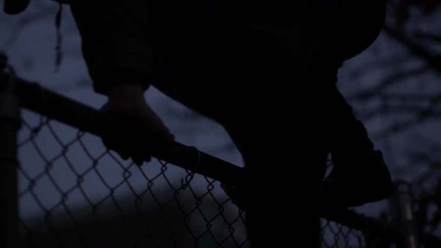 Person climbing a chain-link fence in the dark