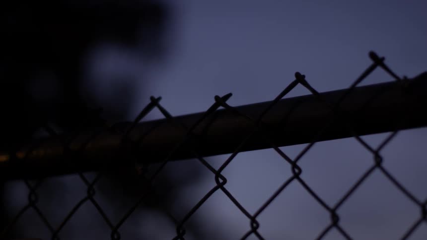 Person climbing a chain-link fence in the dark