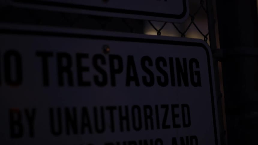 A no trespassing sign hangs on a fence at night