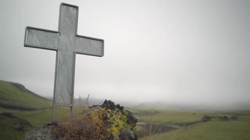 A cross sitting atop a rock on a foggy day