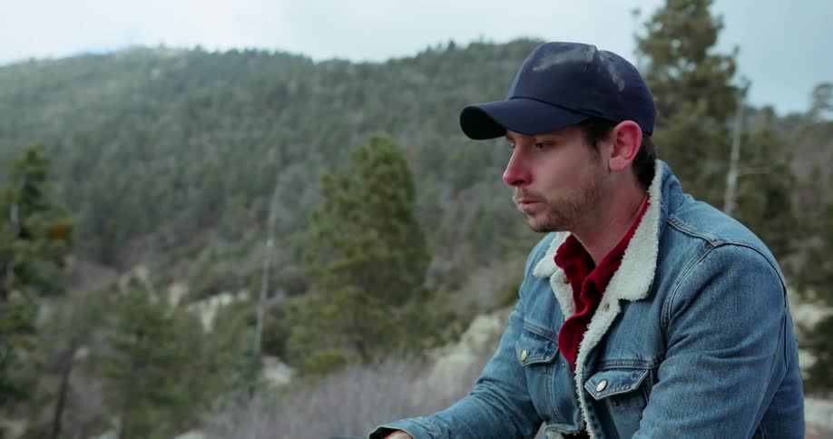 A man peels an apple and takes a bite in the mountains