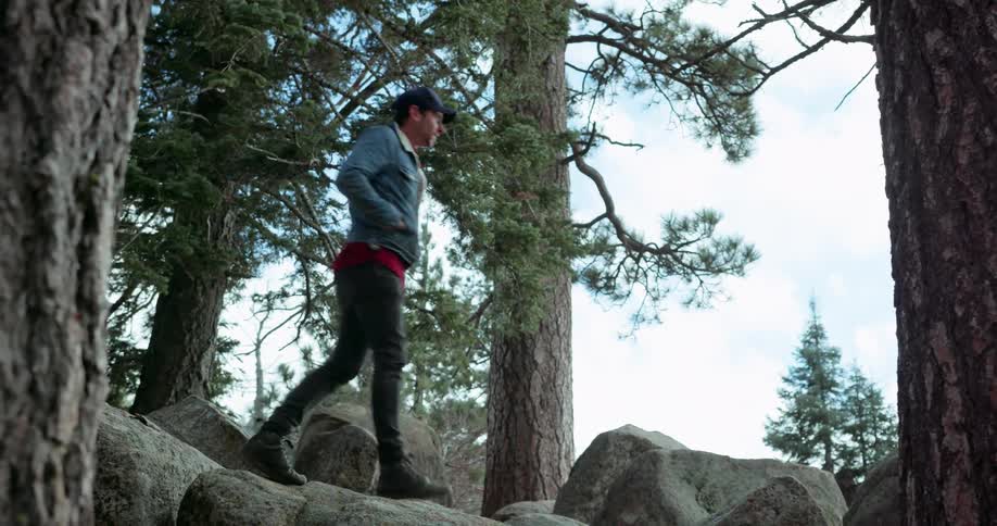 A man hikes down some rocks in a forest
