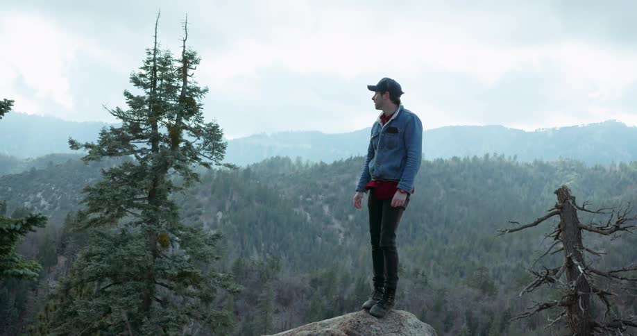 Man stands on top of a rock looking out at the mountains