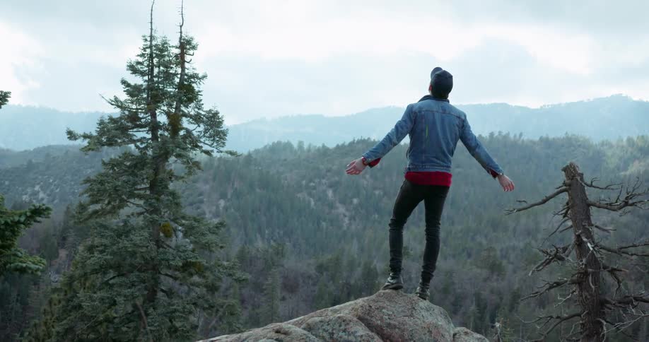 Man stands on mountain top and extends his arms