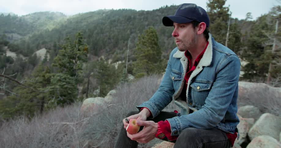 A man is sitting on the edge of a rock eating an apple
