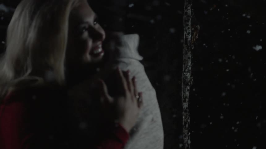 Woman hugs man as snow falls at night