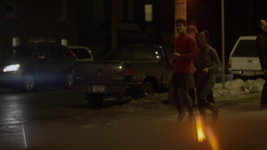 A man and woman jog in place as they wait at an intersection