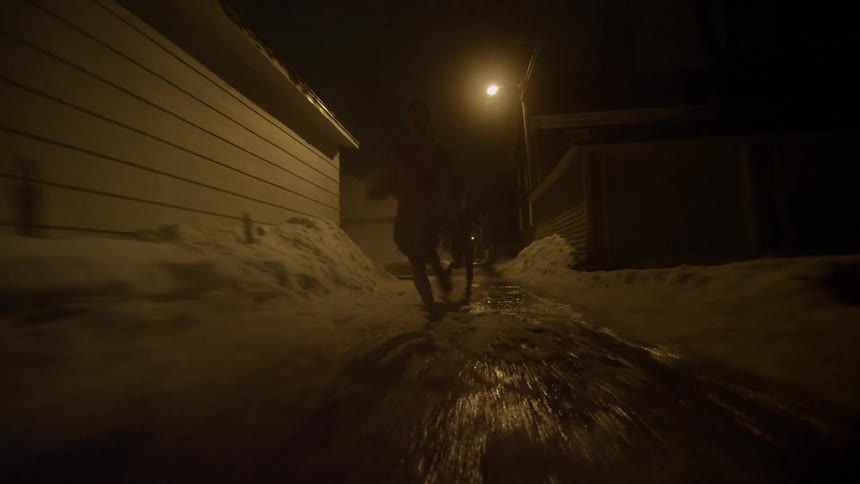 Man and woman run outside in a snowy alley at night