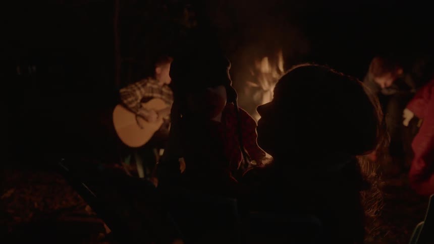 People sitting around a campfire one playing a guitar at night