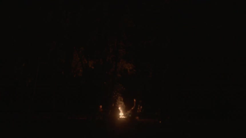 Blurry view of people sitting by a campfire in the dark