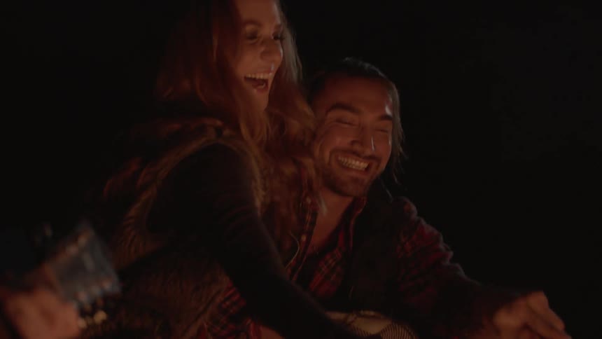 A person is hugging and singing alongside a campfire