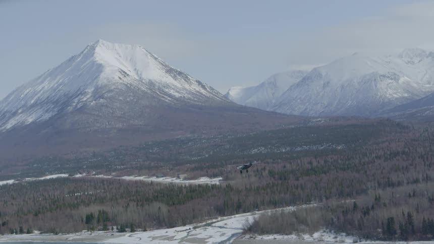 A small airplane flies near snow-covered mountains