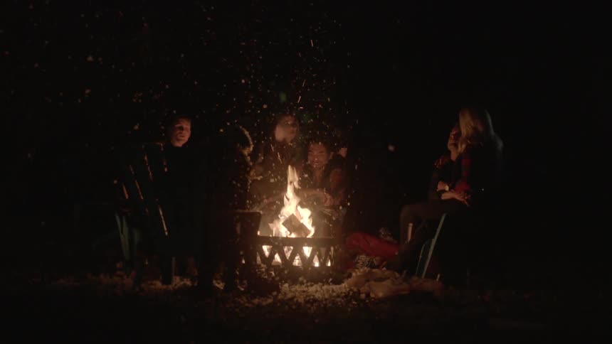 Group of adults sitting around a campfire at night