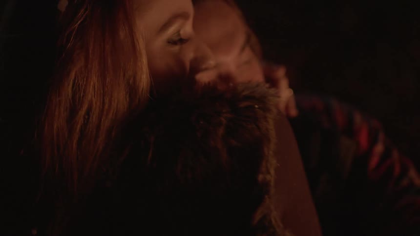 A man and woman hug near a fire at night