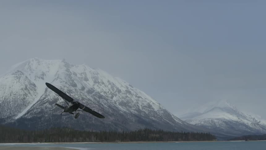 plane takes off by large mountain near a lake with snow on top