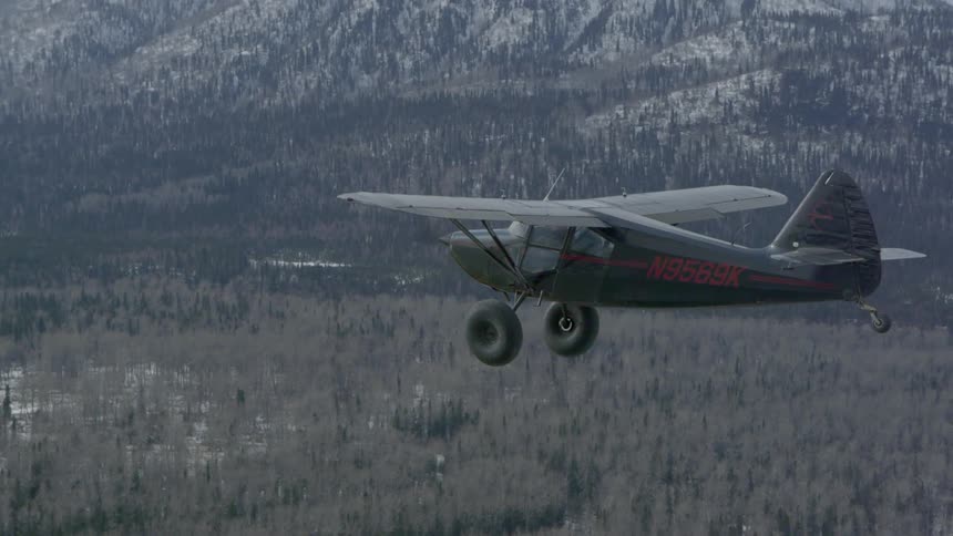 A small airplane flies over a forest and mountain